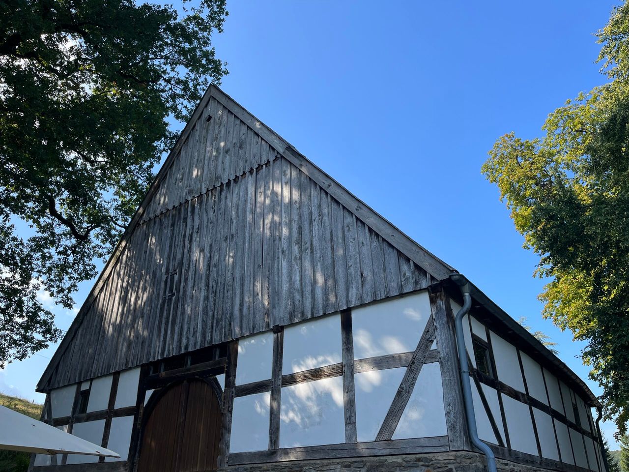 Fachwerk-Bauernhaus mit grauem Holz und weißen Füllungen unter blauem Himmel.