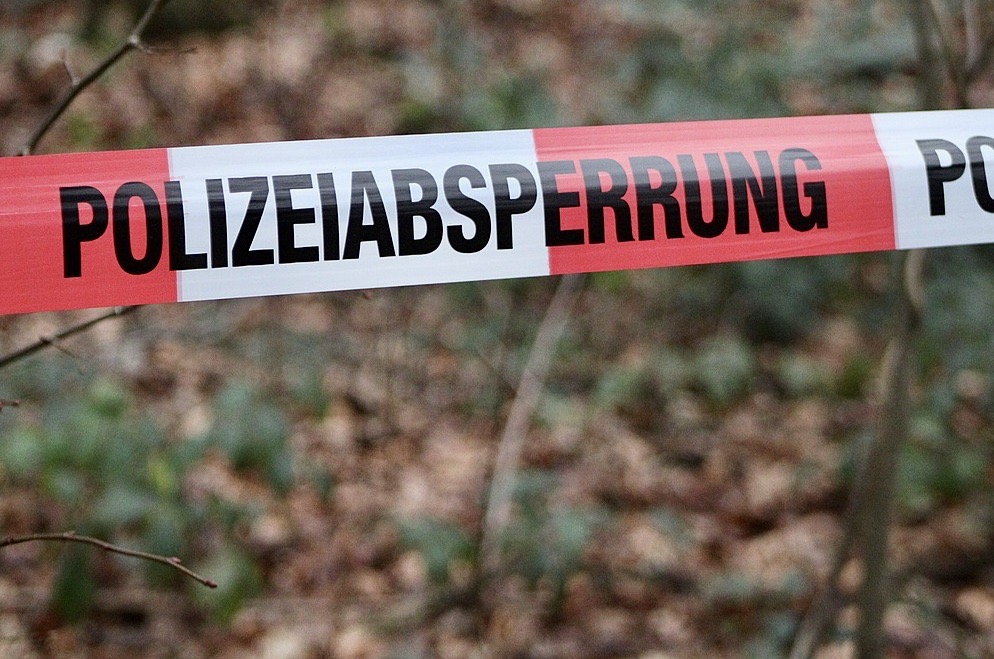 Rotes und weißes Absperrband mit der Aufschrift „POLIZEIABSPERRUNG“ spannt sich vor verschwommenem Unterholz.