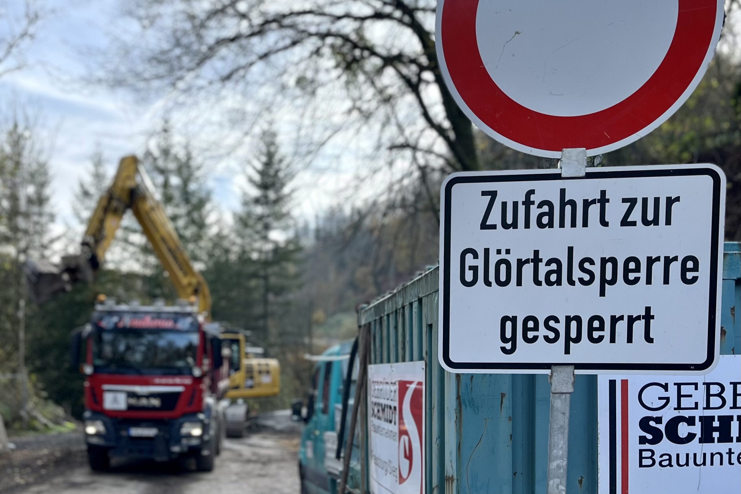 Schild kündigt Sperrung der Zufahrt zur Glörtalsperre an, im Hintergrund ein Bagger und ein Lastwagen auf einer Baustelle.