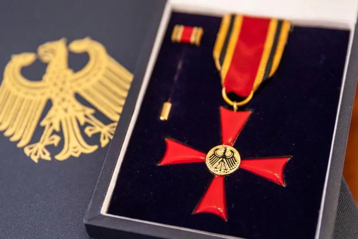 Rotes Verdienstkreuz mit goldenem Adler-Emblem an einem rot-goldenen Band in einer dunklen Schatulle.