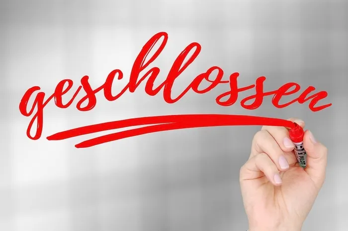 Hand schreibt das Wort „geschlossen“ in roter Farbe auf eine transparente Oberfläche.
