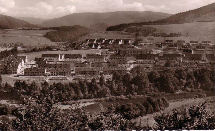 Ein Blick auf die Eschenschule und die umgebenden Gebäude im Jahr 1957, umgeben von Bäumen und Hügeln. Im Vordergrund ist ein Flusslauf zu erkennen.