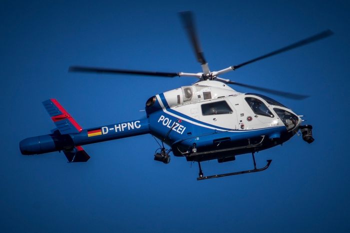 Weiß-blauer Polizeihubschrauber mit dem Schriftzug „POLIZEI“ und der Kennung „D-HPNC“ fliegt vor blauem Himmel.
