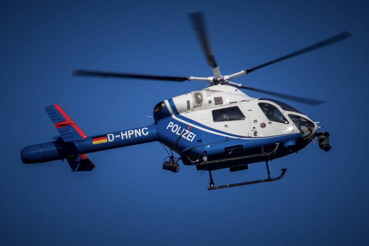 Weiß-blauer Polizeihubschrauber mit dem Schriftzug „POLIZEI“ und der Kennung „D-HPNC“ fliegt vor blauem Himmel.
