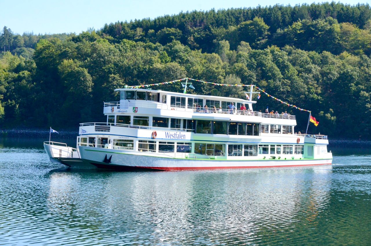 Das weiße Passagierschiff Westphalen fährt auf dem Biggesee vor einer bewaldeten Uferlandschaft.