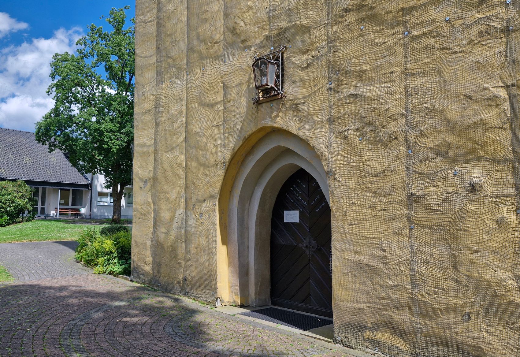 Der Haupteingang der Servatiuskirche mit einem Spitzbogen und einer verzierten Laterne über dem Portal. Die Fassade ist mit einem Maschendrahtnetz abgedeckt.