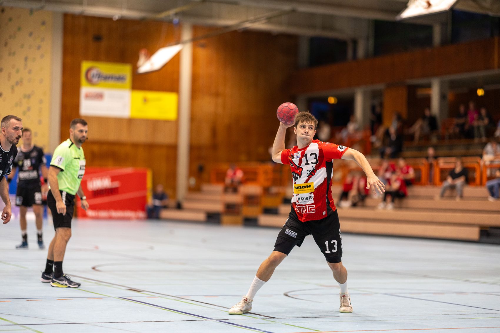 Handballspieler Erik Blaauw mit rotem Trikot und der Nummer 13 wirft den Ball während eines Spiels in einer Sporthalle.