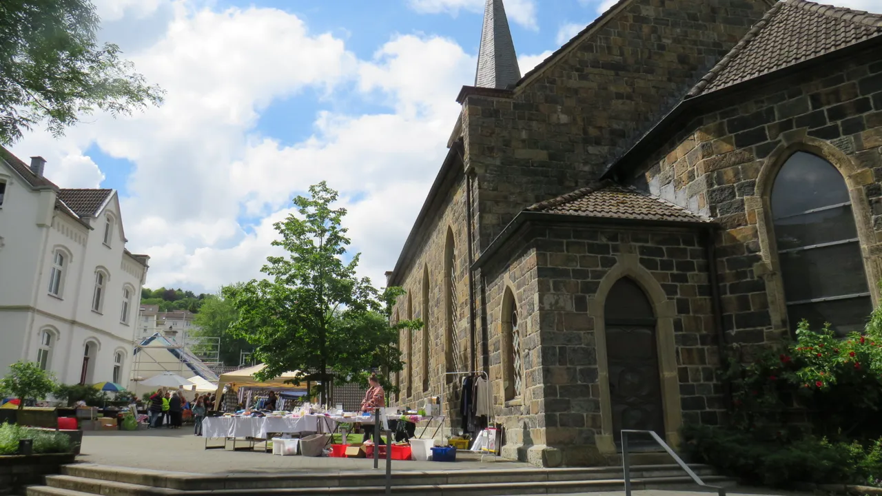 Die Erlöserkirche in Schalksmühle mit einem Markt vor der Fassade an einem sonnigen Tag.