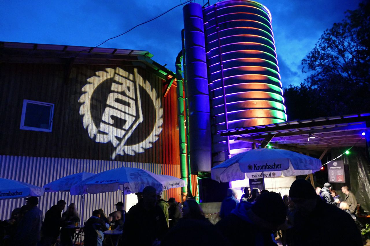 Beleuchtete Silos und ein Gebäude mit dem I-Rock-Festival-Logo im Hintergrund, Menschenmenge vor der Bühne.