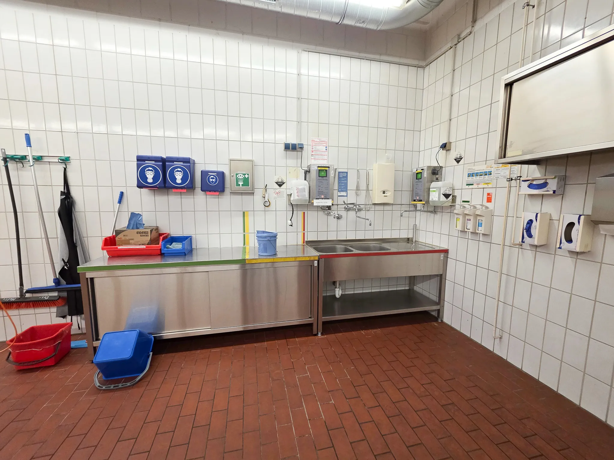 Edelstahl-Waschbecken und Reinigungsausrüstung in einer hellen, gefliesten Halle zur Fahrzeugreinigung.