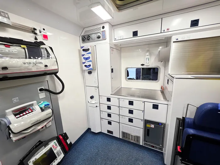 Innenraum eines Rettungswagens mit medizinischer Ausrüstung an der Wand und Schränken, bereit für den Transport eines Patienten ins Krankenhaus.