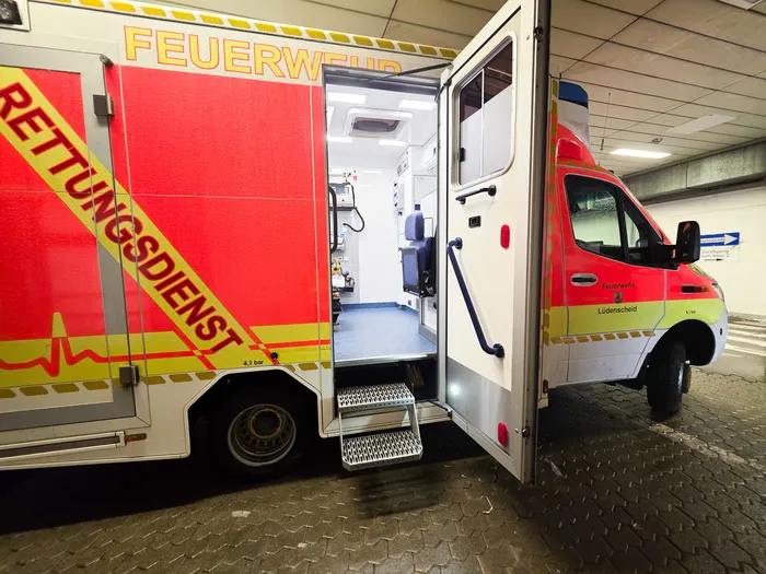 Offener Rettungswagen mit geöffneter Hecktür, der medizinische Ausrüstung und eine Trage zeigt. Auf dem Fahrzeug sind die Aufschriften „Feuerwehr“ und „Rettungsdienst“ zu sehen.
