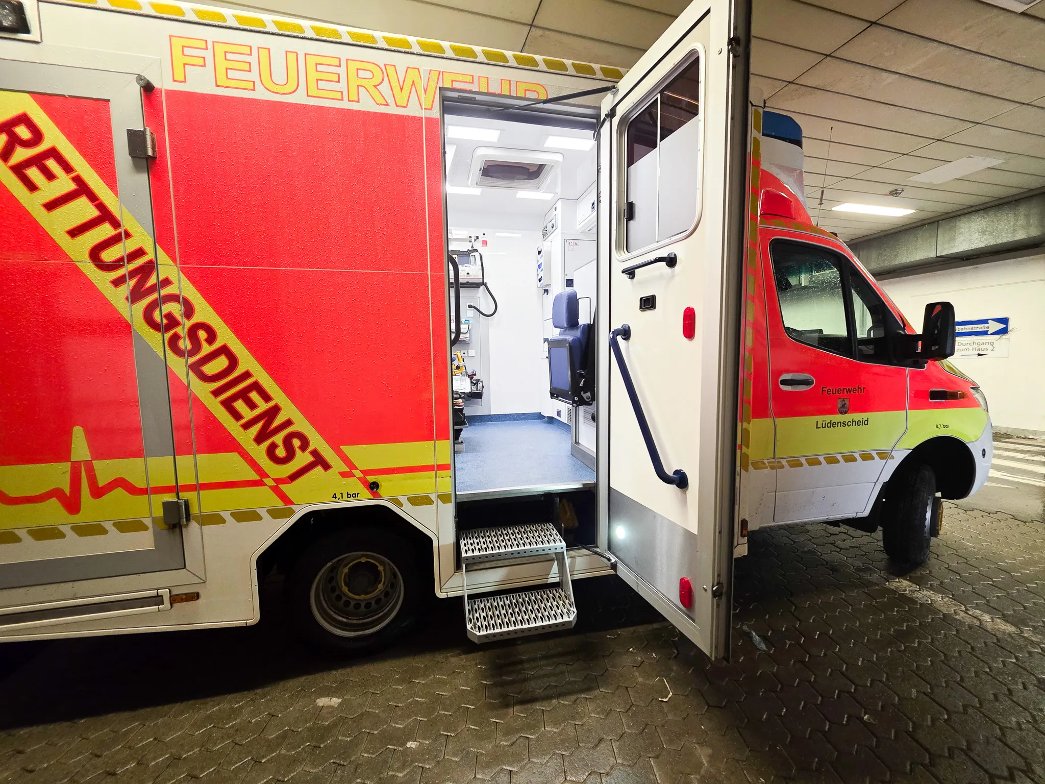 Offener Rettungswagen mit geöffneter Hecktür, der medizinische Ausrüstung und eine Trage zeigt. Auf dem Fahrzeug sind die Aufschriften „Feuerwehr“ und „Rettungsdienst“ zu sehen.