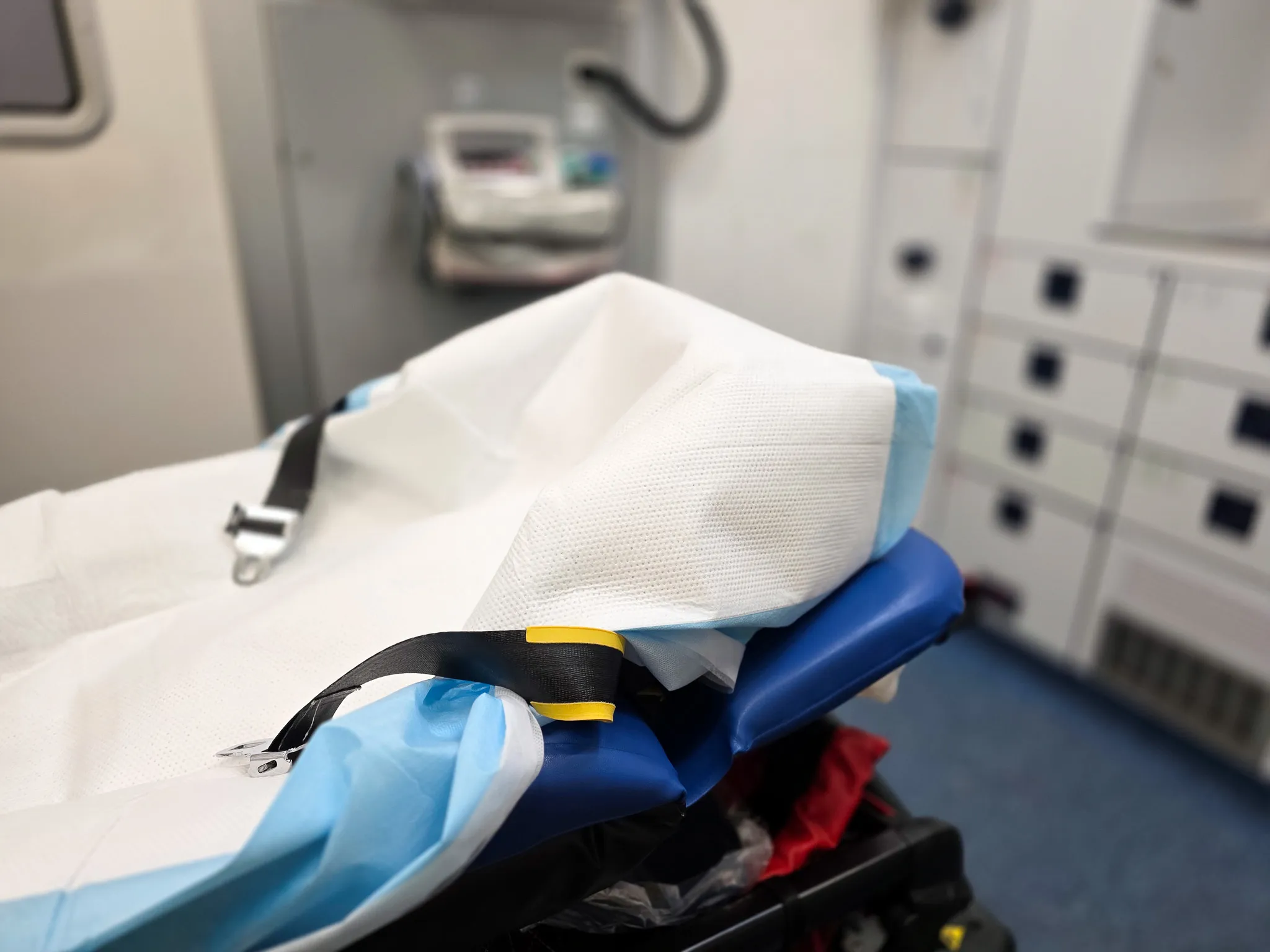 Ein Tragebett mit weißer und blauer Abdeckung im Inneren eines Rettungswagens, medizinische Geräte im Hintergrund.