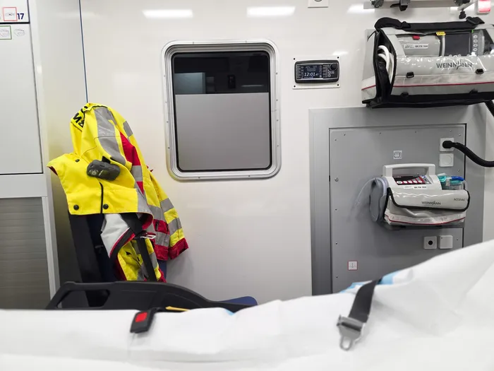 Innenansicht eines Rettungswagens mit medizinischer Ausrüstung und einer gelben Jacke, die an einer Halterung hängt.