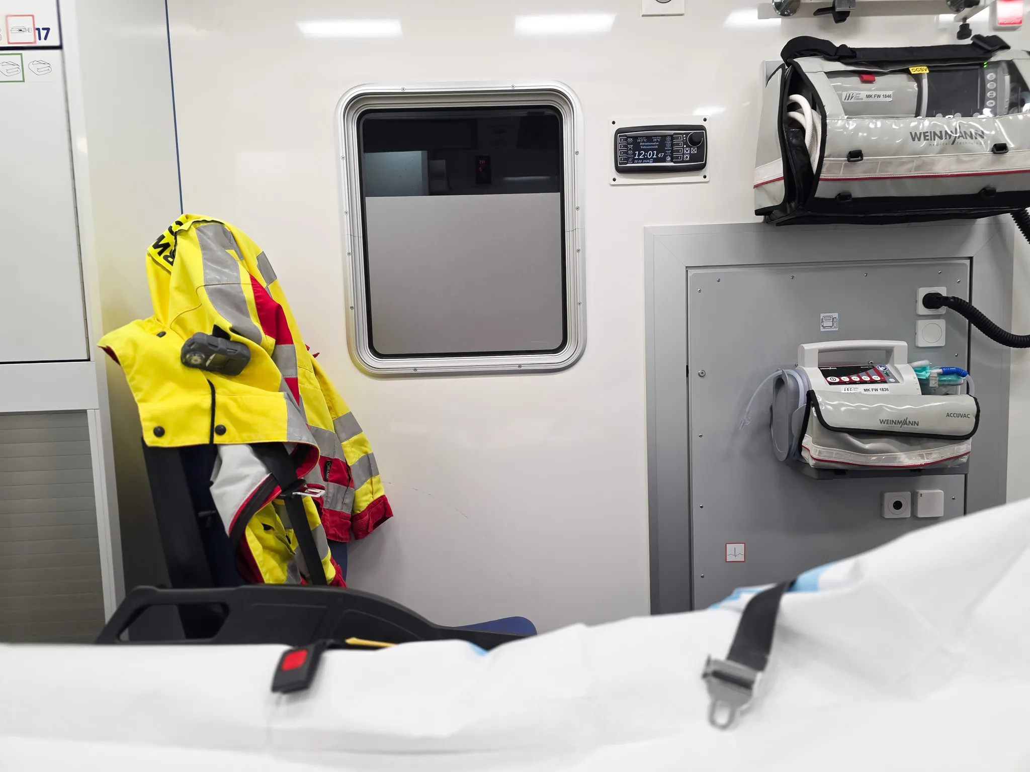 Innenansicht eines Rettungswagens mit medizinischer Ausrüstung und einer gelben Jacke, die an einer Halterung hängt.