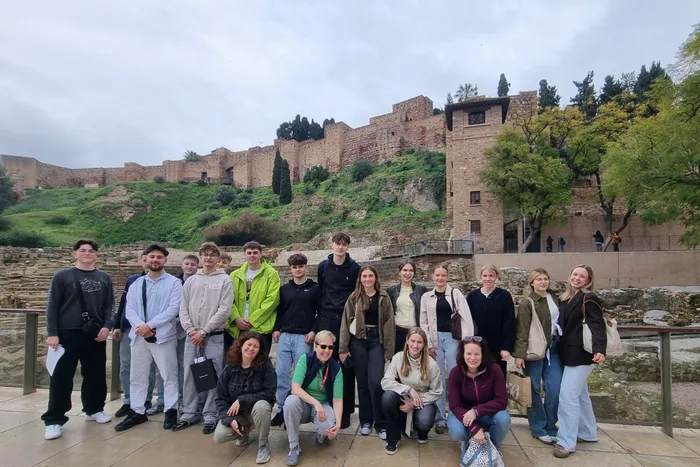 Eine Gruppe junger Menschen steht vor einer mittelalterlichen Burg in Málaga, Spanien, im Rahmen eines beruflichen Praktikums.