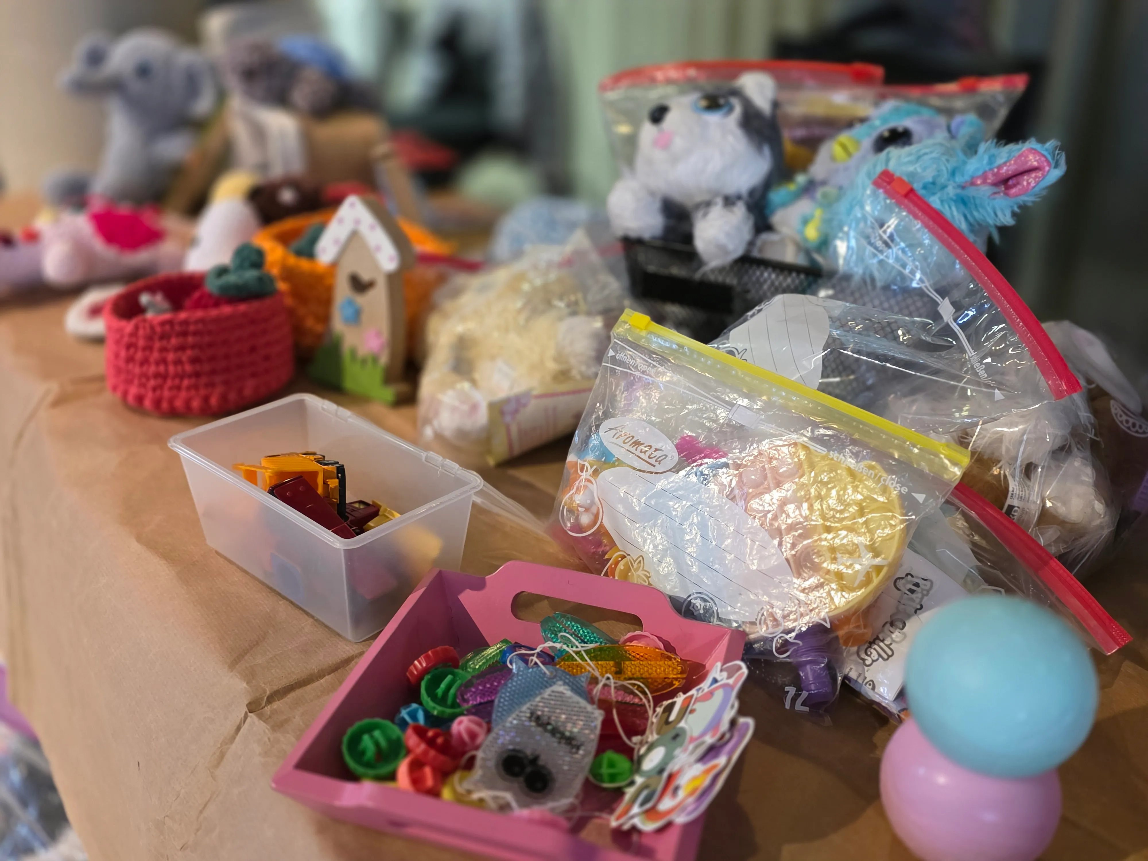 Verschiedenes Spielzeug, darunter Stofftiere, kleine Figuren und Zubehör, ist auf einem Tisch ausgelegt und teilweise in Plastiktüten verpackt.