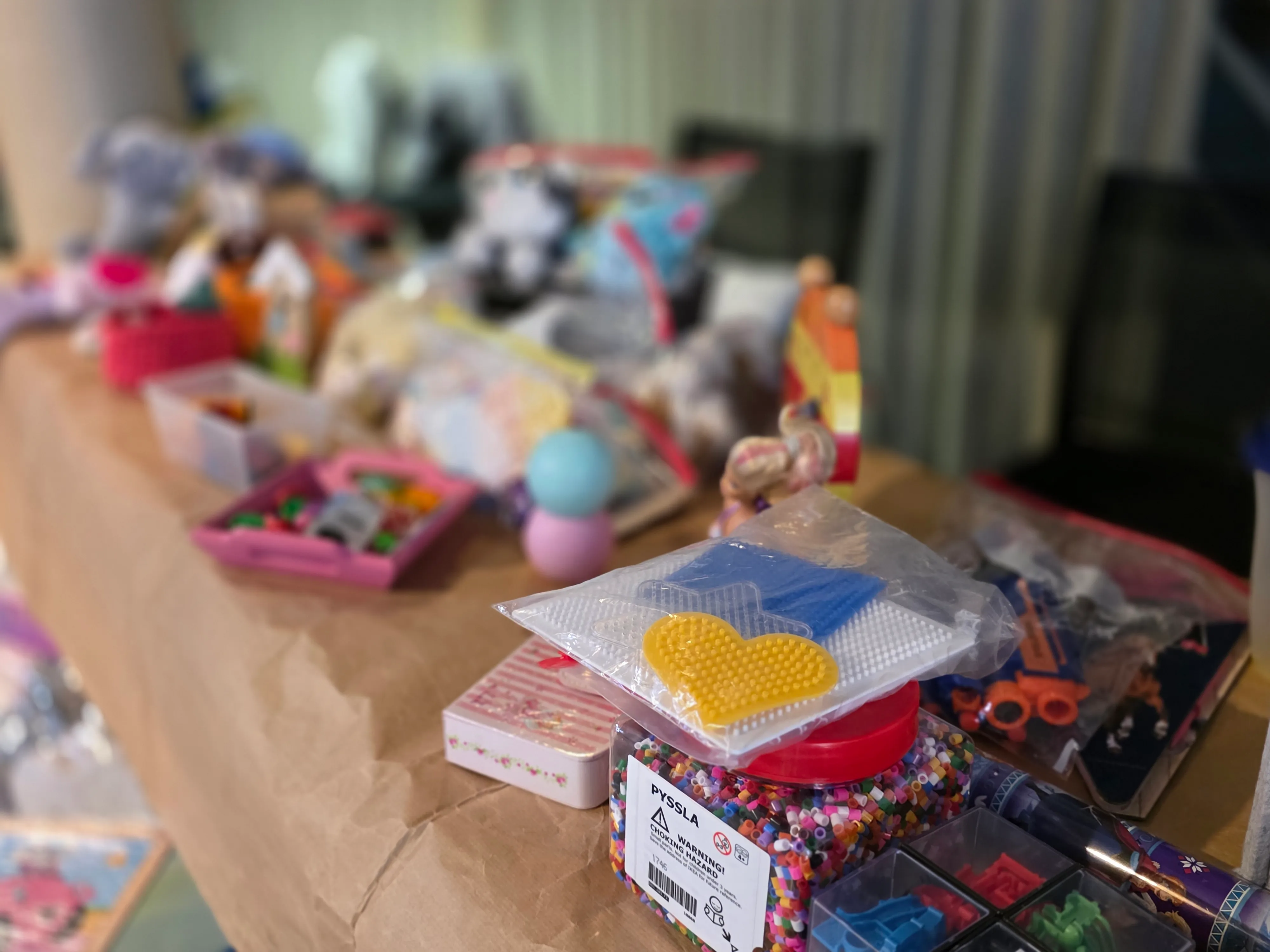 Spielzeug, darunter Figuren, Baukästen und Perlen, auf einem Tisch in einem Raum mit hellen Wänden.