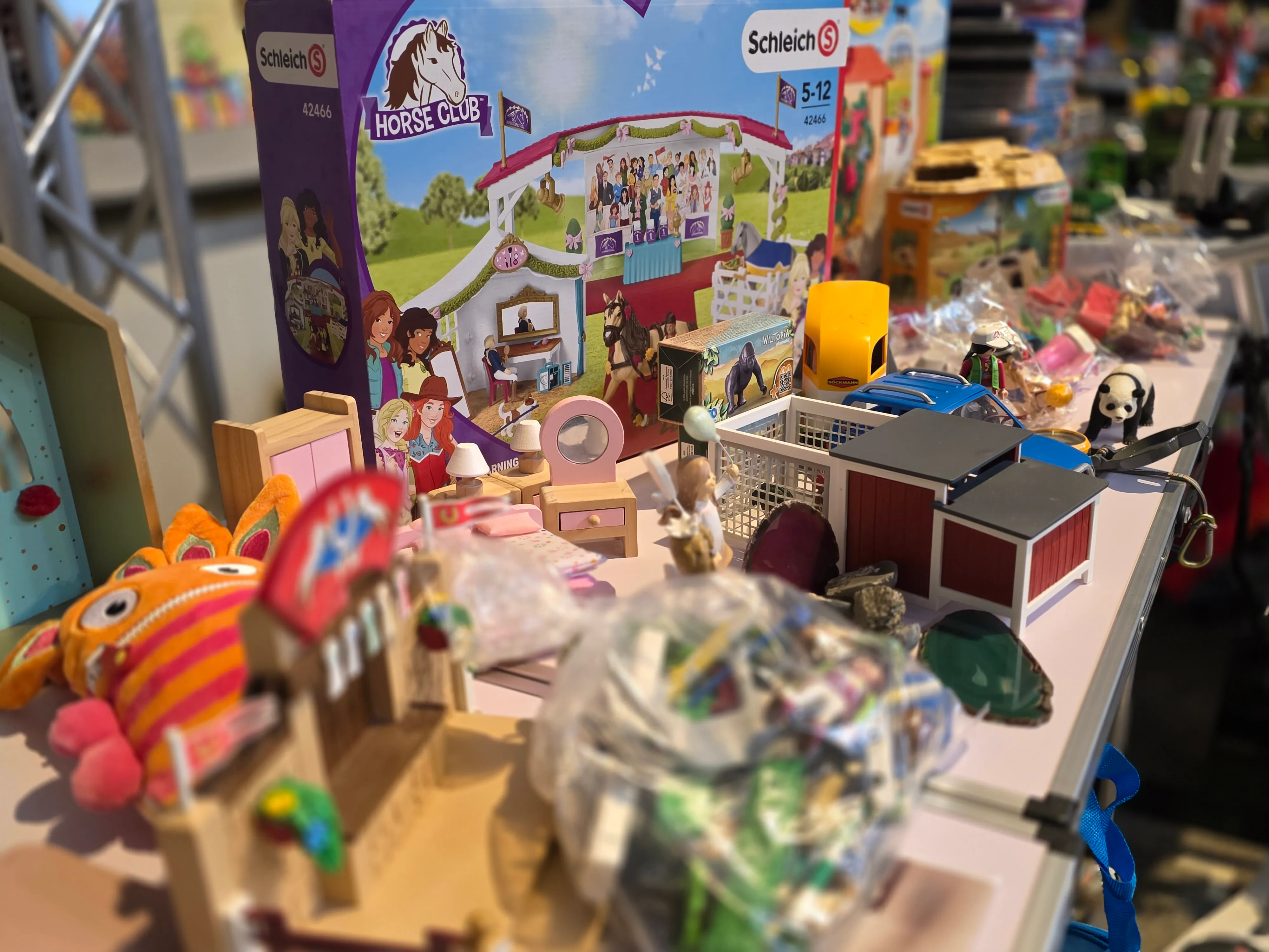 Schleich-Figuren und ein Horse Club Spielset stehen auf einem Tisch, umgeben von anderem Spielzeug auf einer Spielzeugbörse.