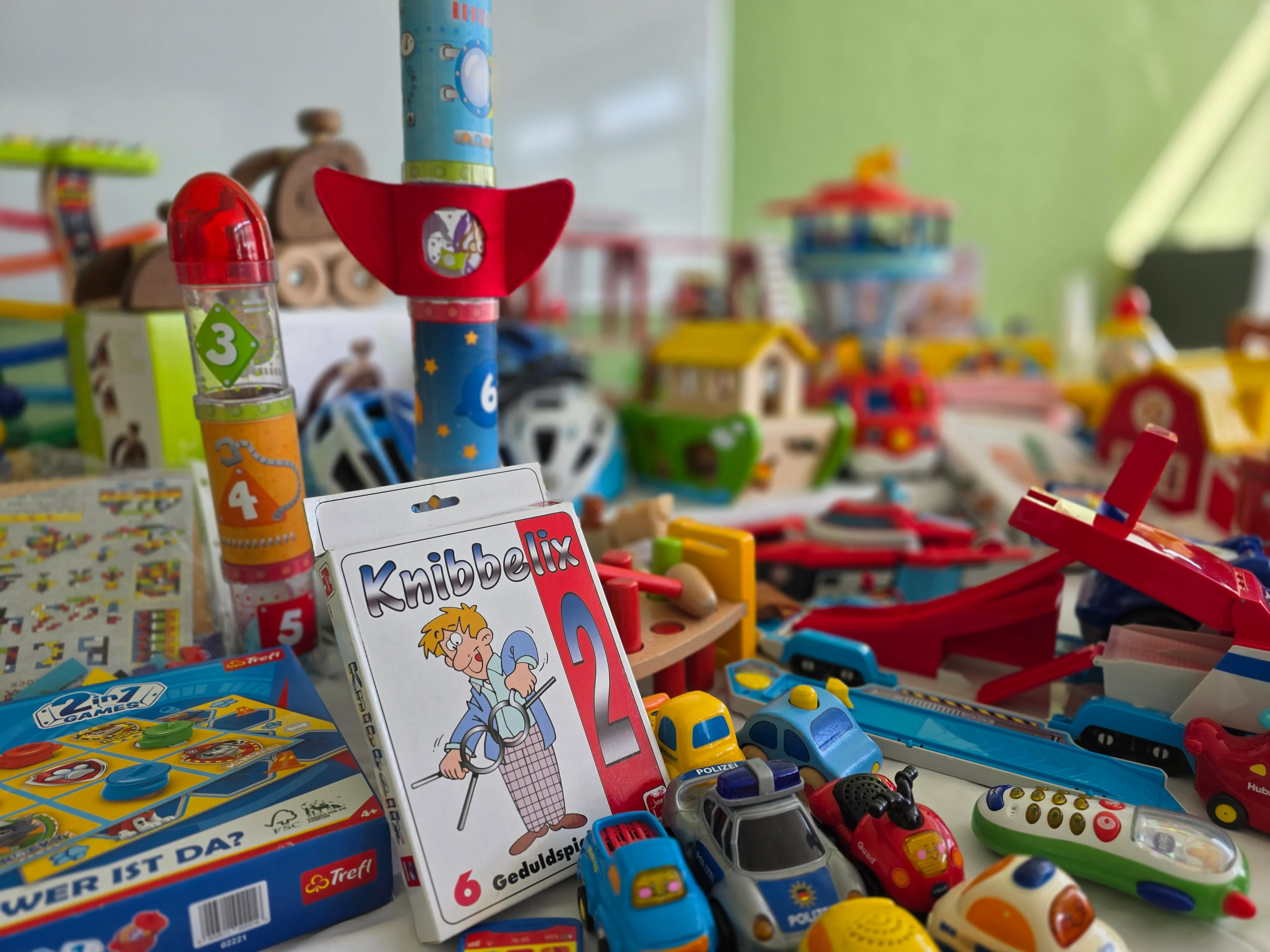 Buntes Spielzeug auf einem Tisch, darunter Raketen, Autos und das Gesellschaftsspiel Knibbelix.