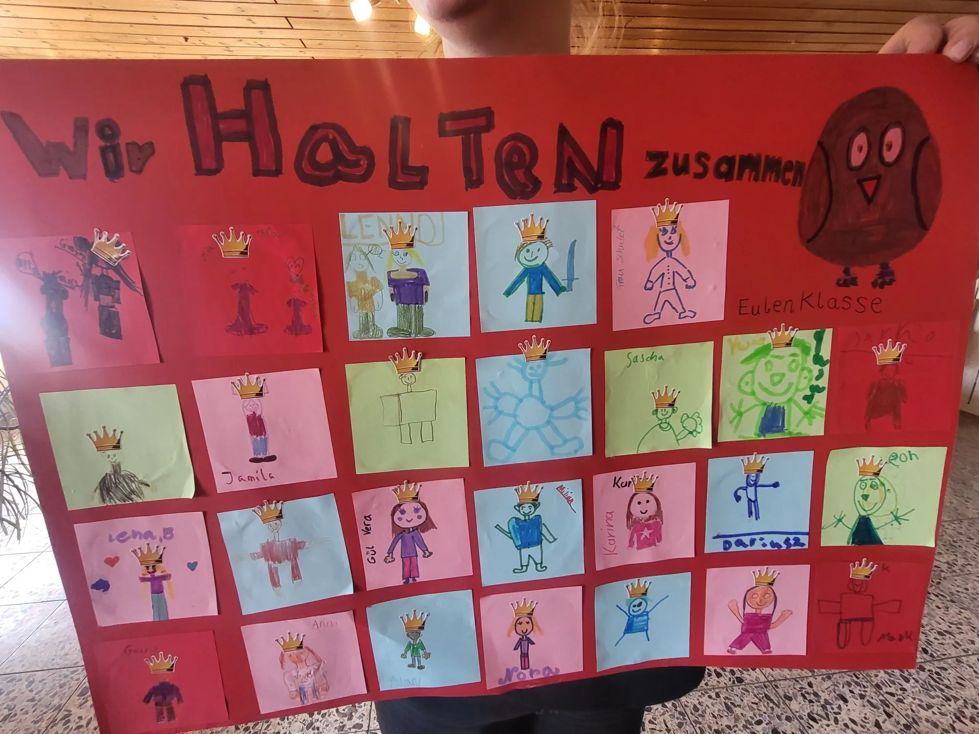Eine Collage aus Kinderzeichnungen mit gekrönten Figuren und Herzen, beschriftet mit „Wir Halten Zusammen“ und „Eulen Klasse“.