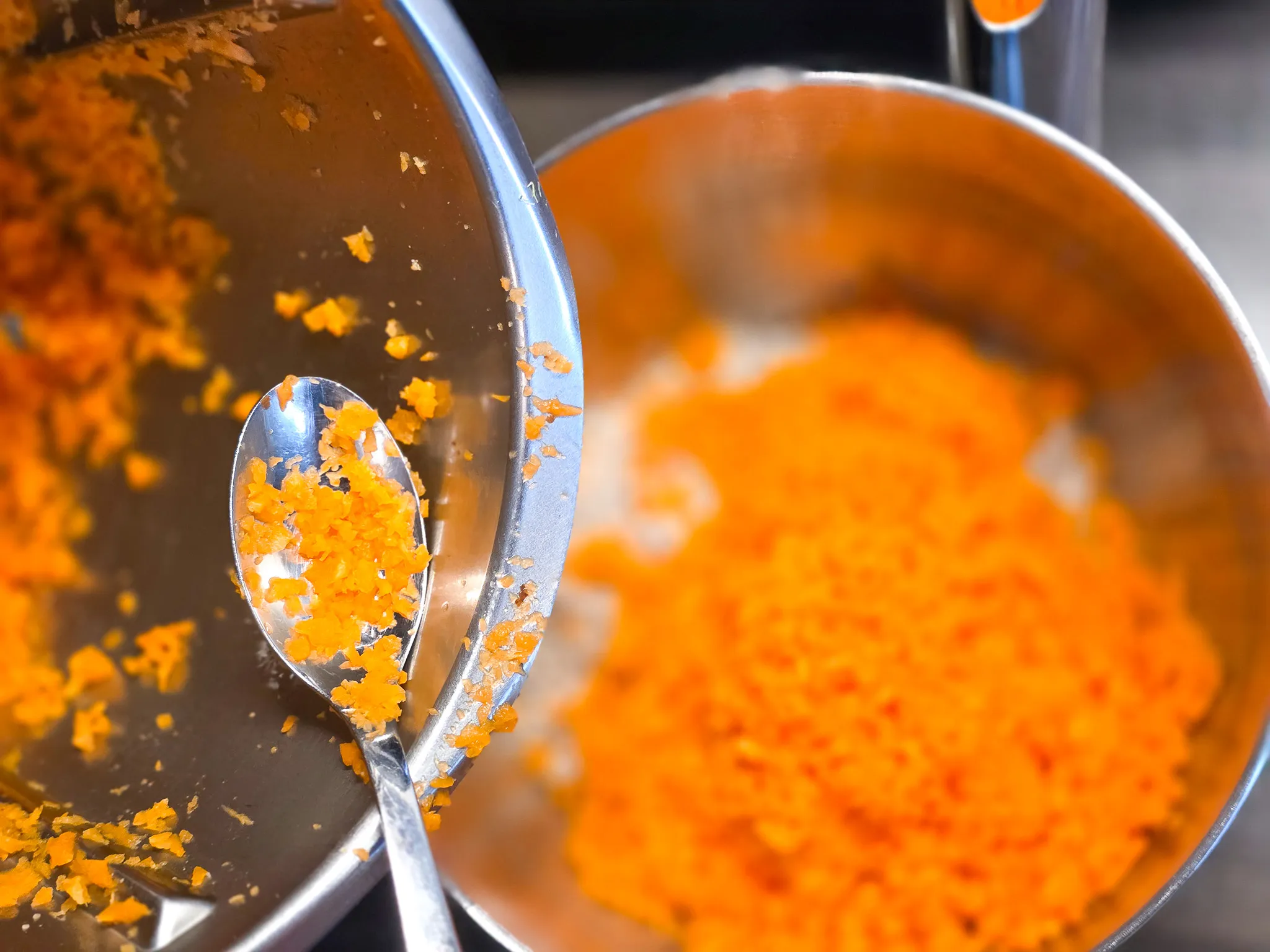 Geriebene Karotten in einer Edelstahlschüssel und auf einem Löffel, Zutaten für einen Karottenkuchen.