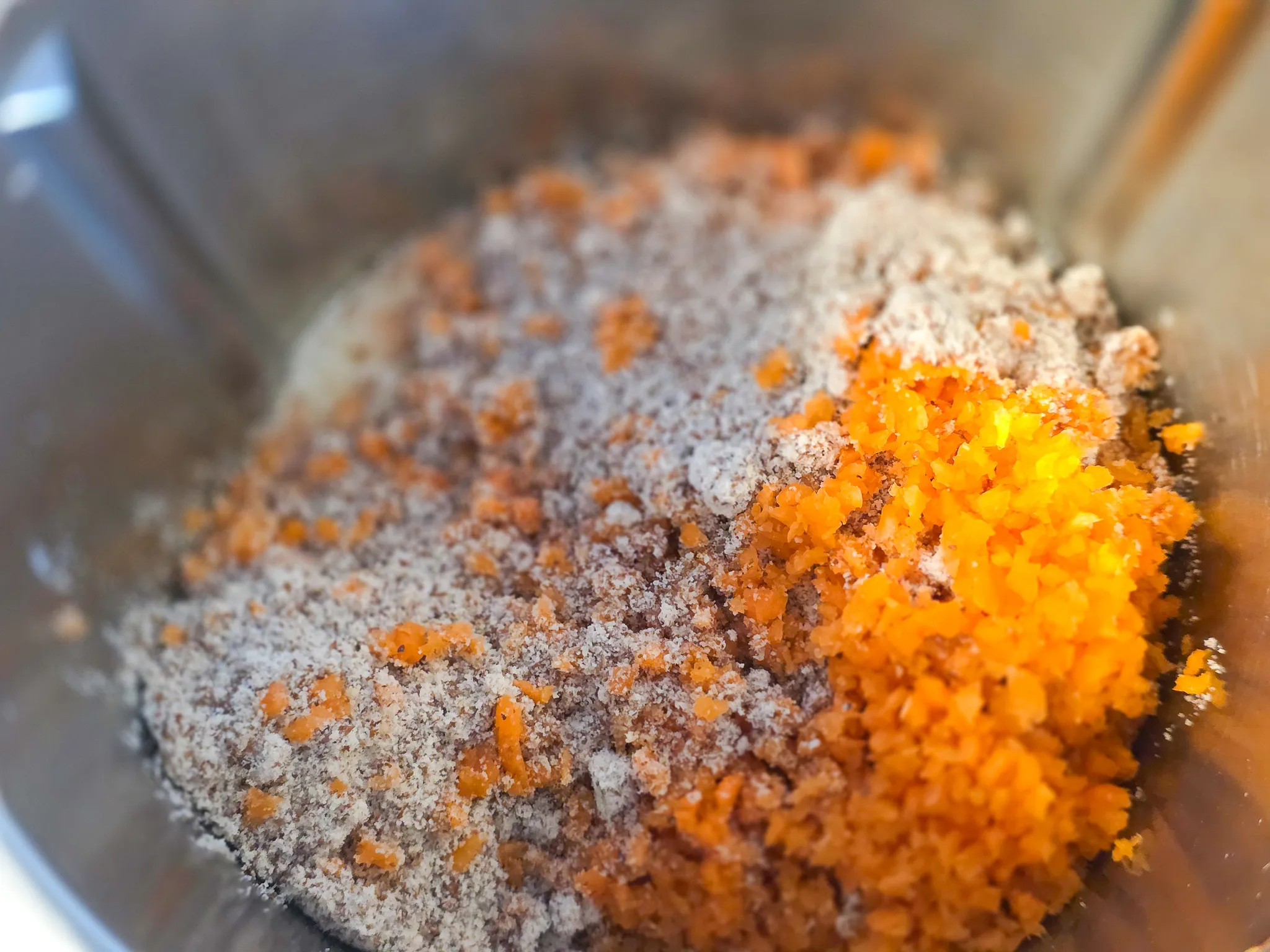 Gemisch aus geriebener Karotte, Mehl und weiteren Zutaten in einer Metallschüssel, vermutlich für einen Rüblikuchen.