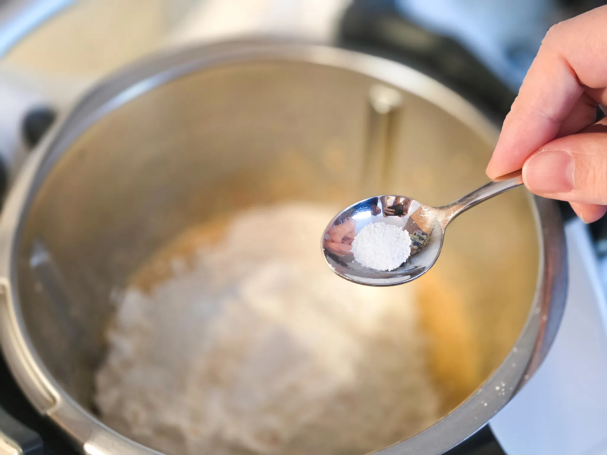 Eine Hand hält einen Teelöffel mit Salz über einen großen Topf mit Teig, vermutlich für einen Karottenkuchen.