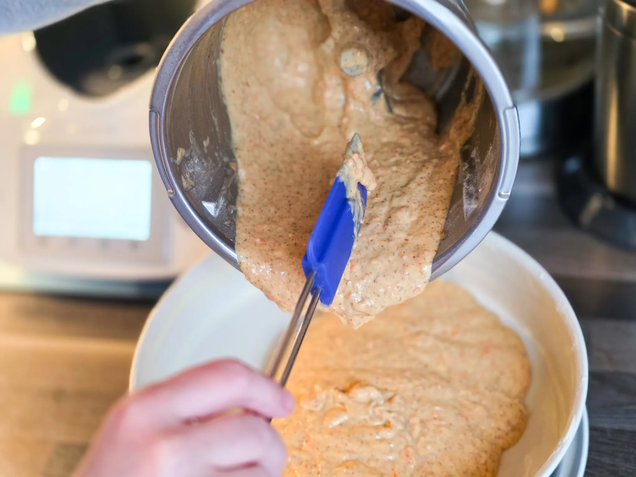 Ein Rübliteig wird aus einem Metallbehälter in eine Schüssel gegossen, ein blauer Spatel hält den Teig fest.