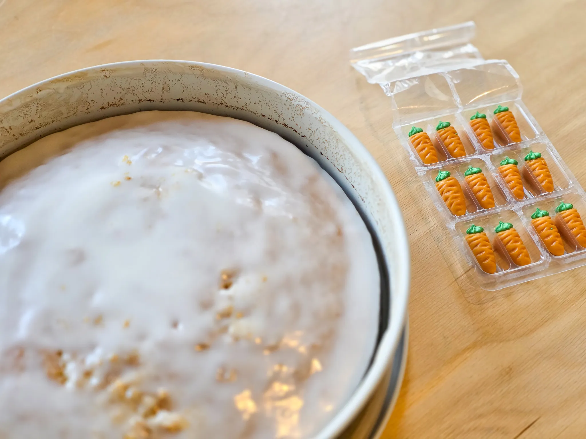 Rüblikuchen mit weißem Guss und Streuseln neben einer Packung kleiner Marzipanrüben.