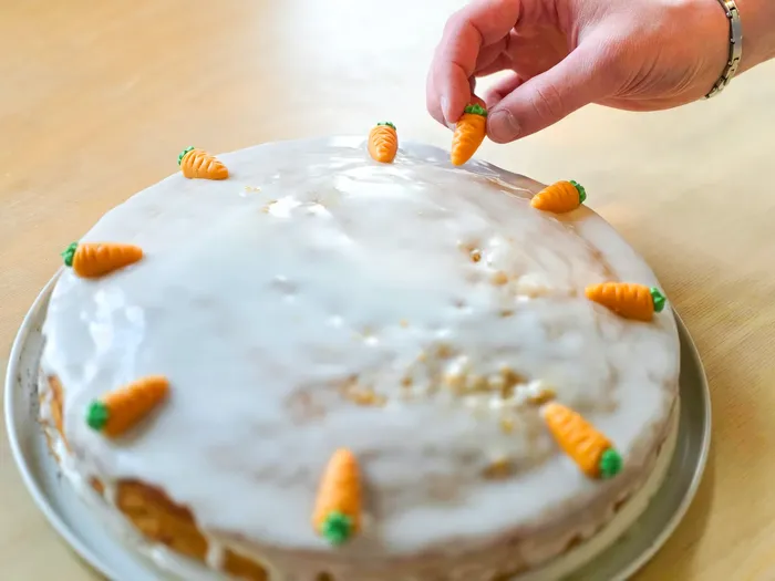 Hand platziert Marzipan-Karotten auf einem mit weissem Guss überzogenen Kuchen.
