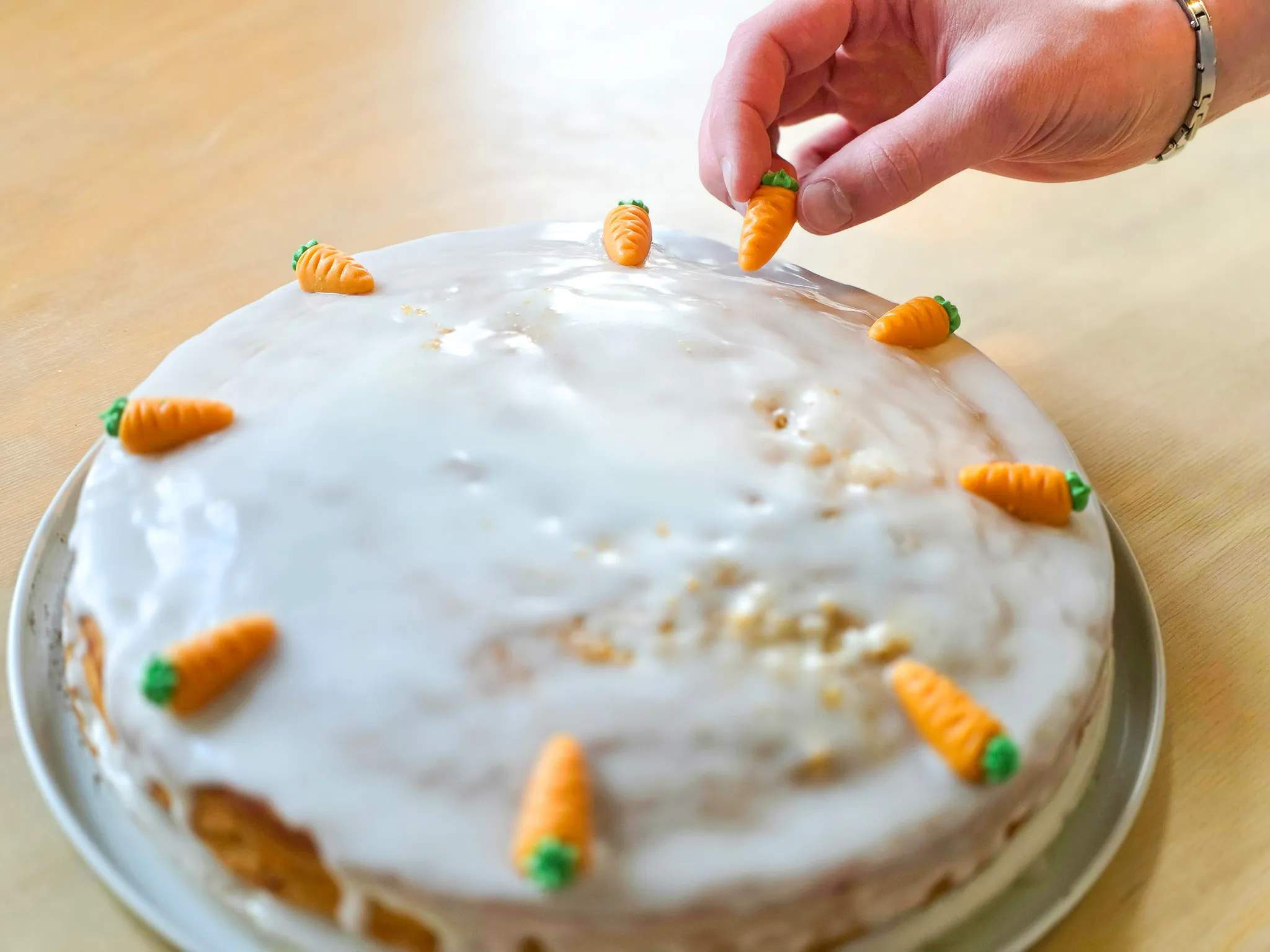 Hand platziert Marzipan-Karotten auf einem mit weissem Guss überzogenen Kuchen.