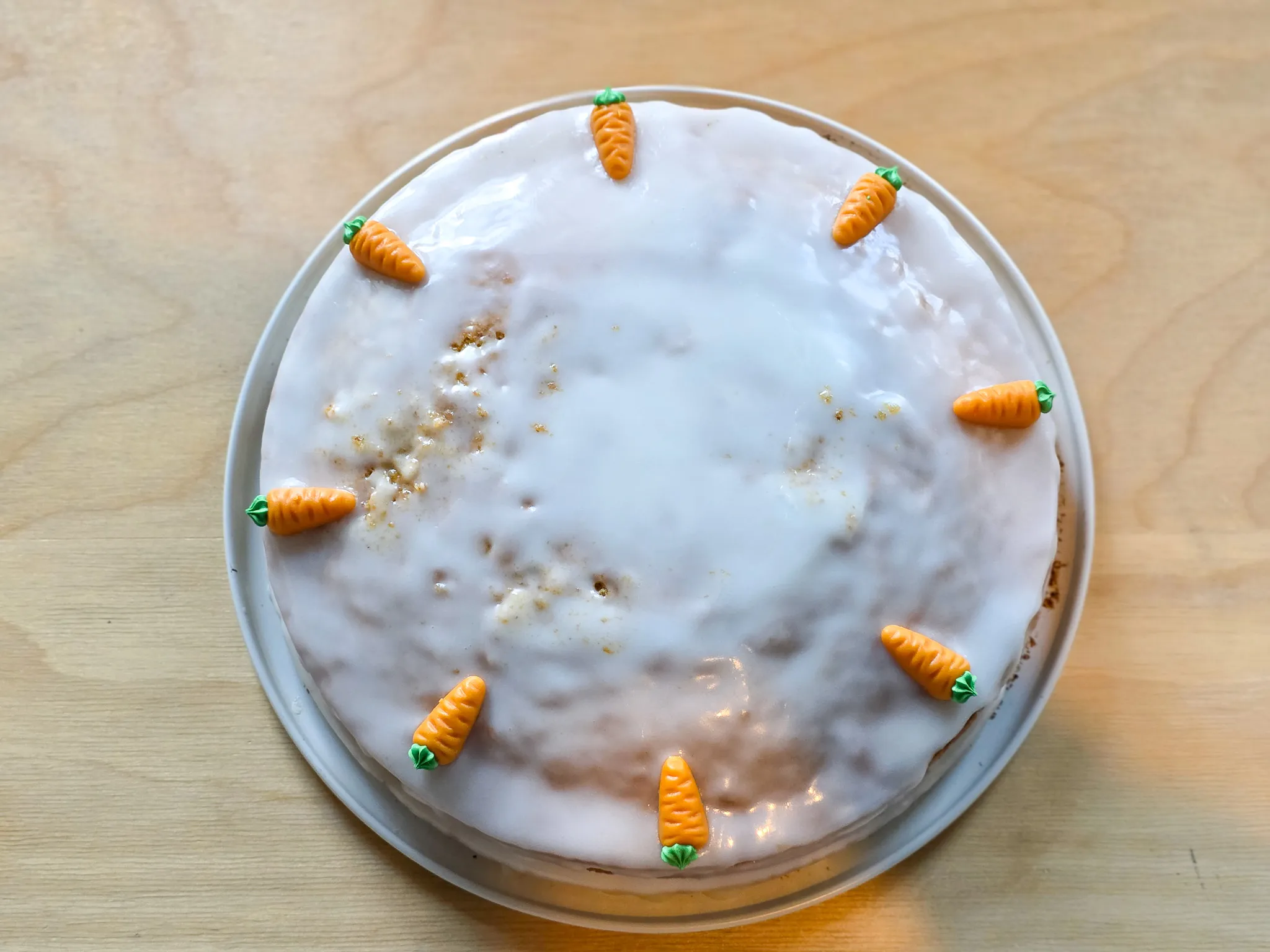 Rund geformter Rüblikuchen mit weißem Guss und kleinen Marzipanrüben als Dekoration.