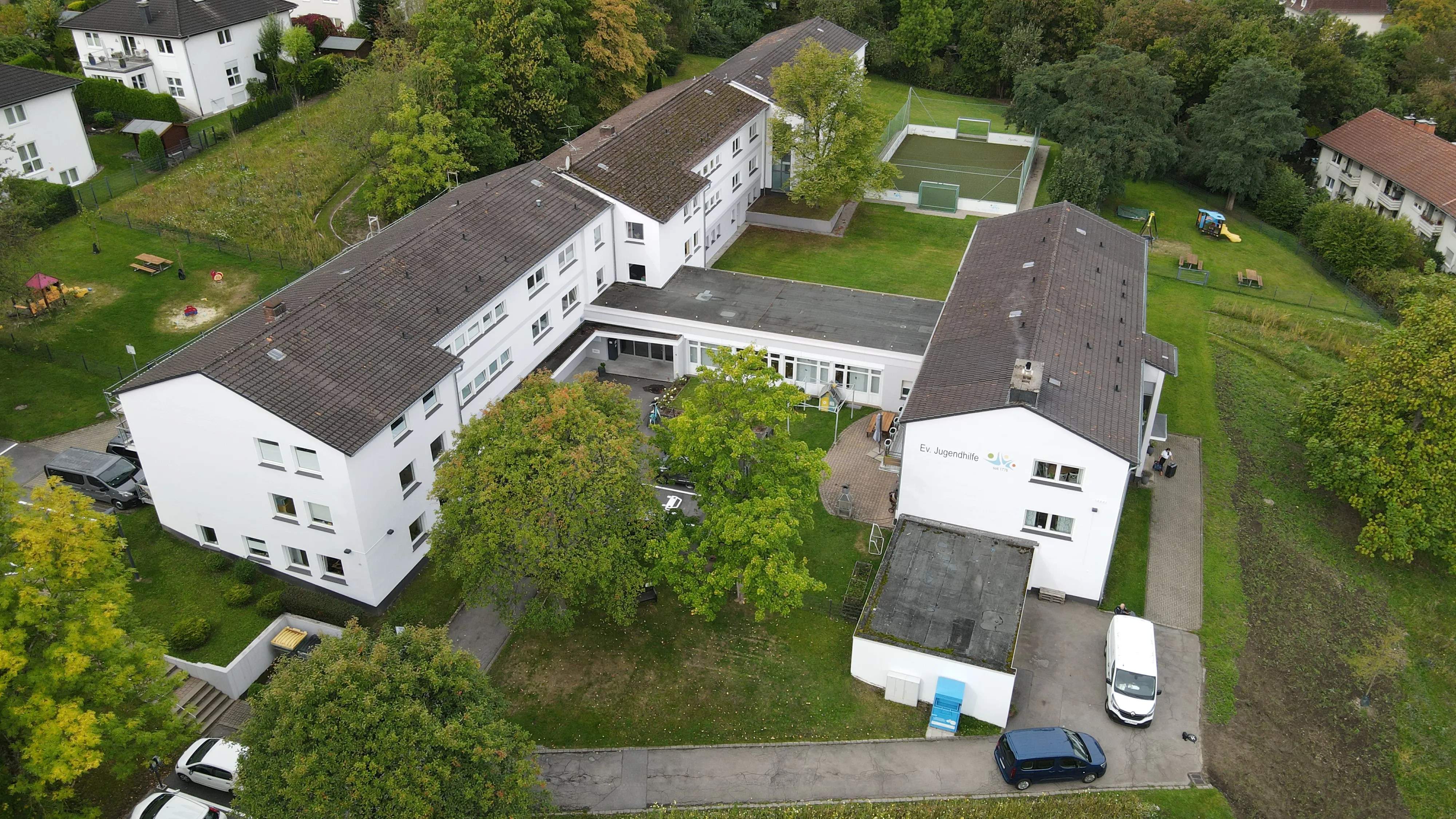 Luftaufnahme des Hauptsitzes der Evangelischen Jugendhilfe Iserlohn-Hagen, ein mehrflügeliger Gebäudekomplex mit gepflegtem Gelände und Parkplätzen.