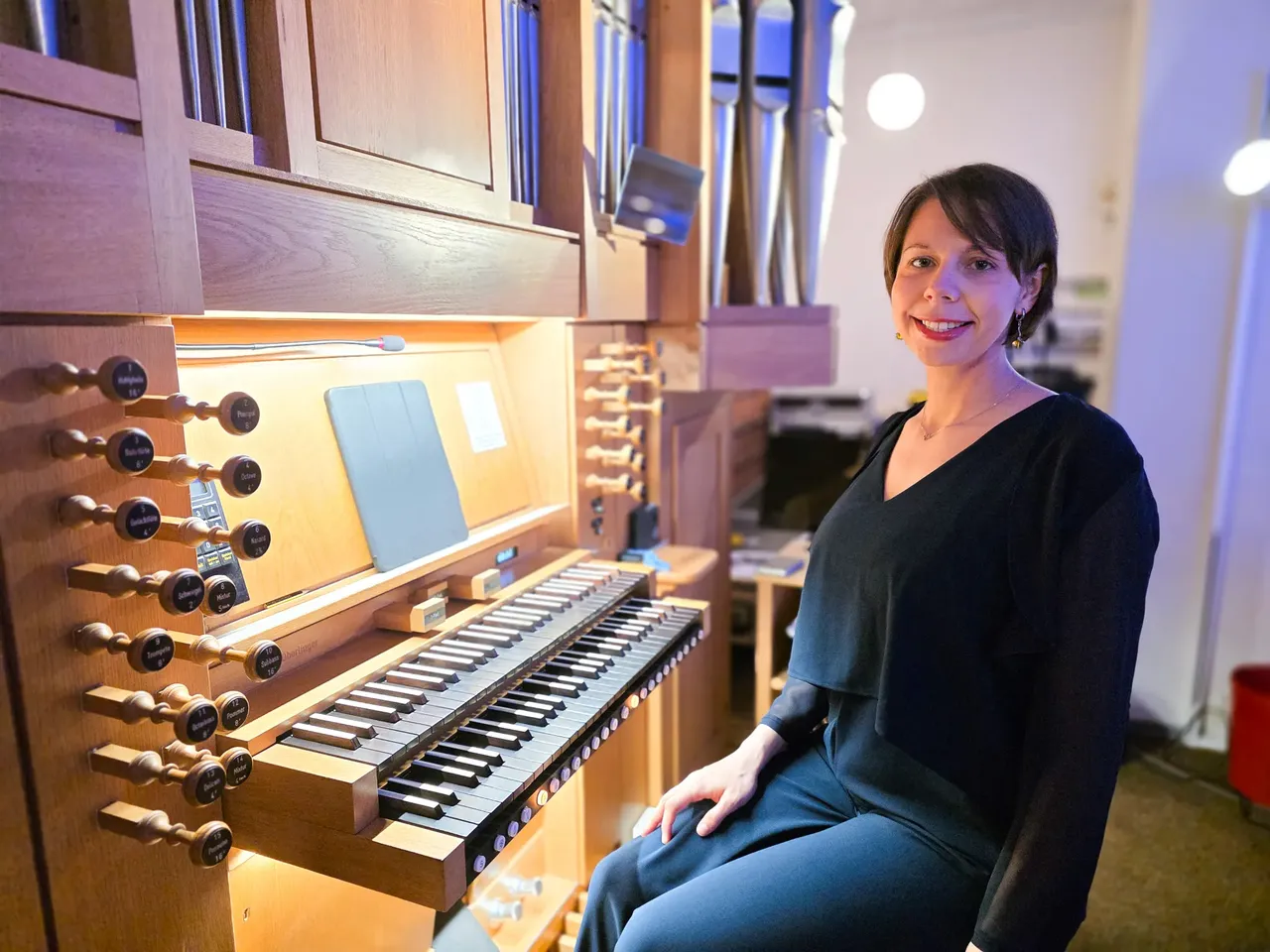 Organistin Julia Chekulaeva sitzt lächelnd vor der Orgel und spielt. Die Orgel hat mehrere Register und ein Klavier.