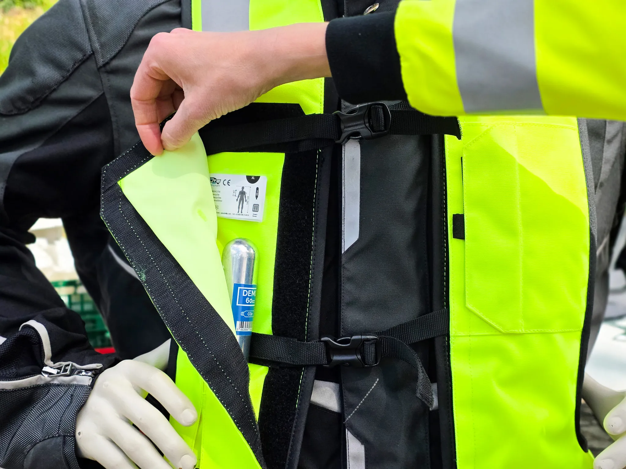 Eine Hand öffnet eine Tasche an einer gelben Warnweste, in der eine Erste-Hilfe-Ausrüstung und eine kleine Gaspatrone zu sehen sind.