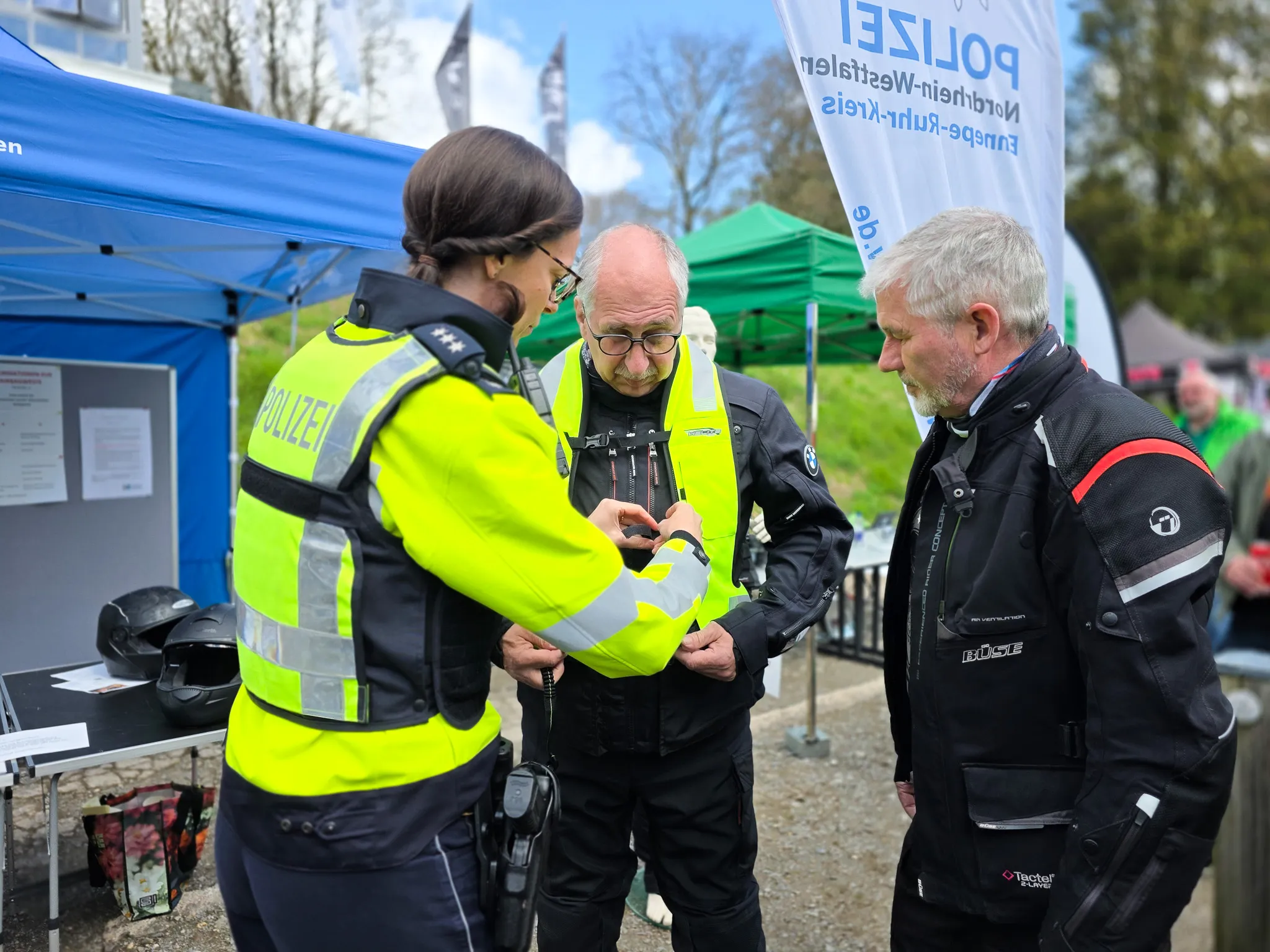 Polizistin erklärt einem älteren Motorradfahrer die Funktionsweise einer Schutzweste bei einer Präventionsveranstaltung.