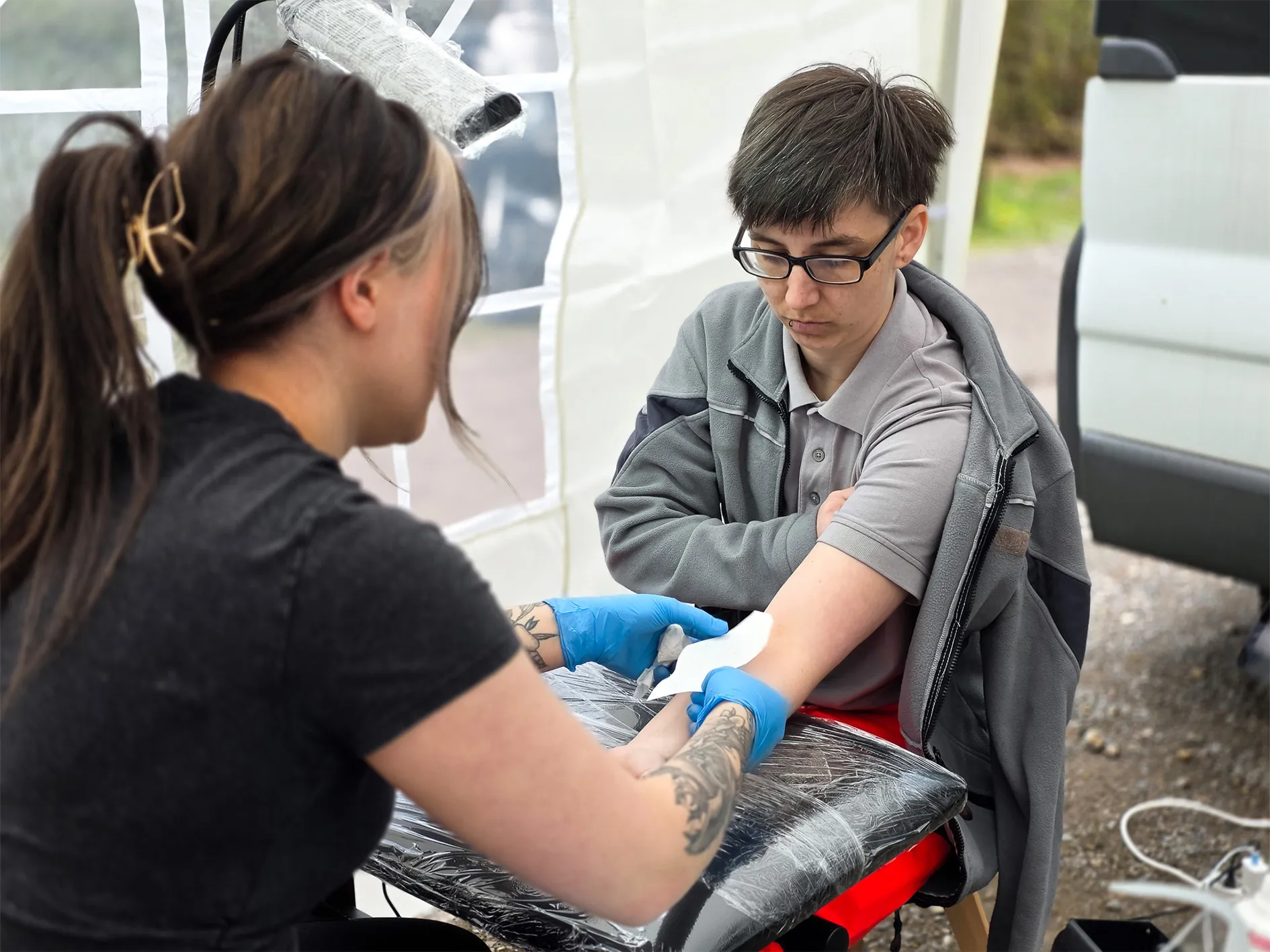 Eine Person erhält während einer Präventionsveranstaltung für Biker von einer Tätowiererin ein temporäres Tattoo auf den Unterarm.