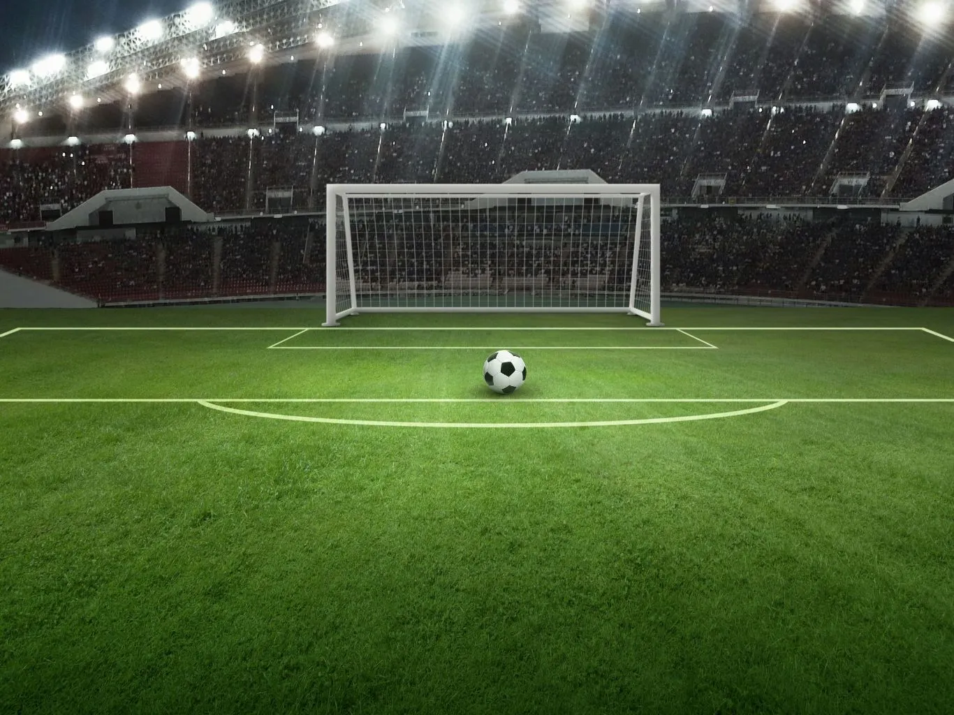 Fußballfeld mit Tor und Ball im Fokus, im Hintergrund ein voll besetztes Stadion bei Nacht.