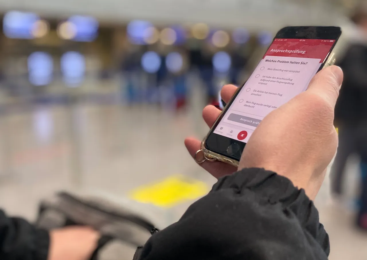 Eine Hand hält ein Smartphone mit einem Formular zur Flugentschädigung. Auf dem Bildschirm sind verschiedene Optionen wie 