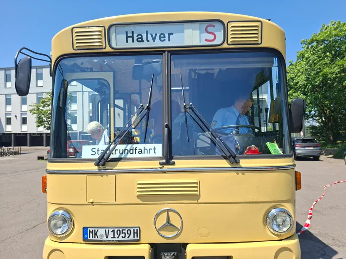 Gelber Oldtimerbus mit dem Ziel „Halver“ und dem Hinweis „Stadtrundfahrt“. Der Fahrer und ein Beifahrer sind im Bus zu sehen.