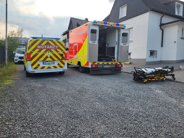 Two emergency vehicles, an ambulance and a smaller response vehicle labeled 'Notarzt' (emergency doctor), are parked on a paved area in front of a white building. The vehicles have yellow and red markings and flashing lights on the roof.