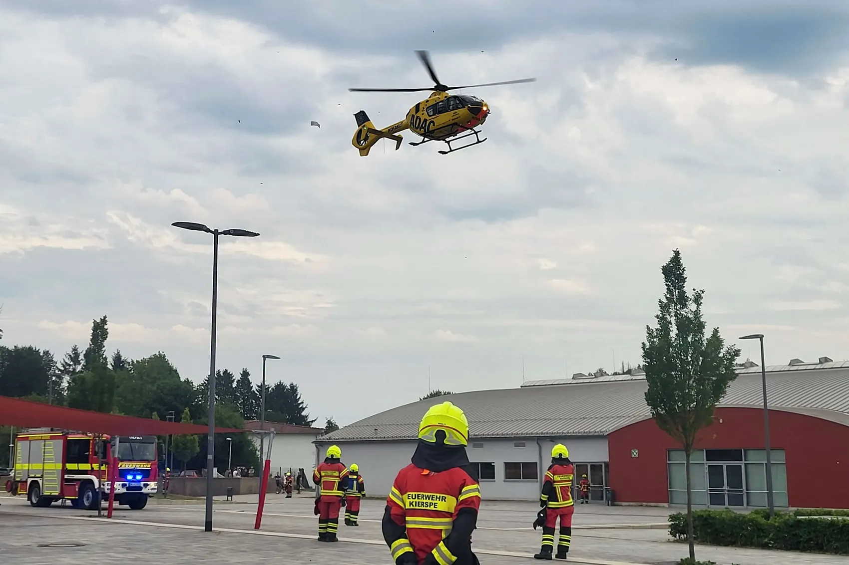 Rettungshubschrauber landet vor einem Feuerwehrgebäude, während Einsatzkräfte in voller Montur bereitstehen.