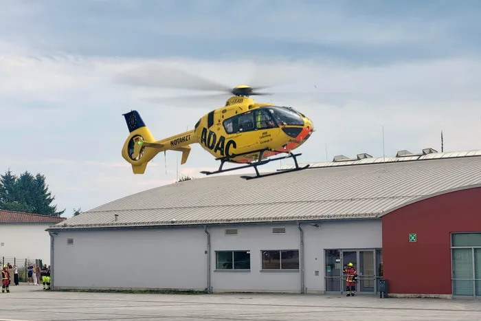 Ein gelber Rettungshubschrauber der ADAC landet auf dem Dach eines flachen Gebäudes, während sich darunter Einsatzkräfte versammeln.