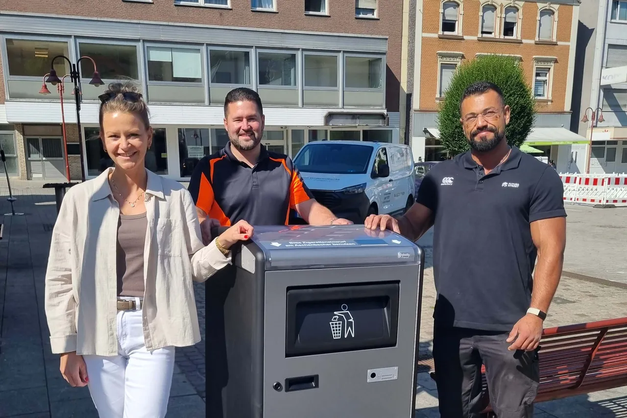 Sabrina Reddemann, Mario Gaentzsch und Kevin Bekaan stehen vor einem grauen, modernen Müllbehälter mit Solarpanel und Sensoröffnung in Ennepetal.