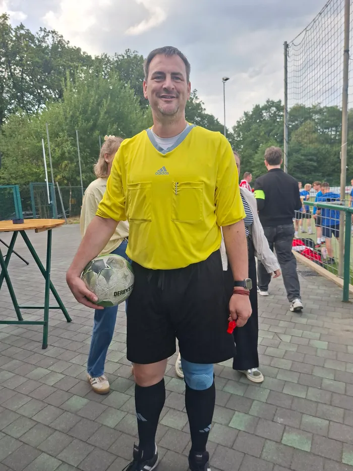 Ein Schiedsrichter in gelbem Trikot hält einen Fußball und eine rote Karte.