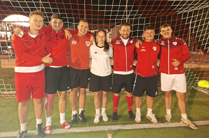 Sieben Personen in roter und weißer Sportkleidung posieren vor einem Fußballtor bei einem Hobby-Fußballturnier.