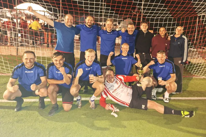 Eine Fußballmannschaft feiert mit einem Pokal und Getränken vor einem Tornetz.