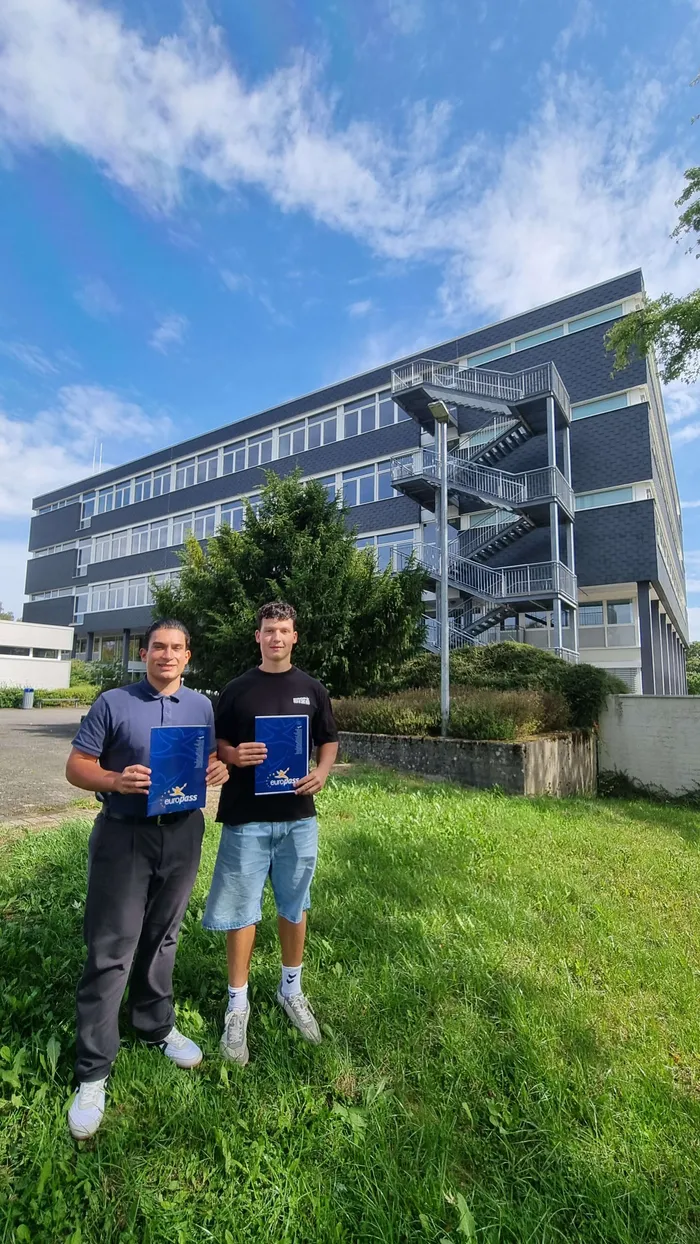 Marc Bober und Giuseppe Trombello stehen vor einem modernen, dunklen Gebäude und halten blaue Mappen mit dem Euroglass-Logo.